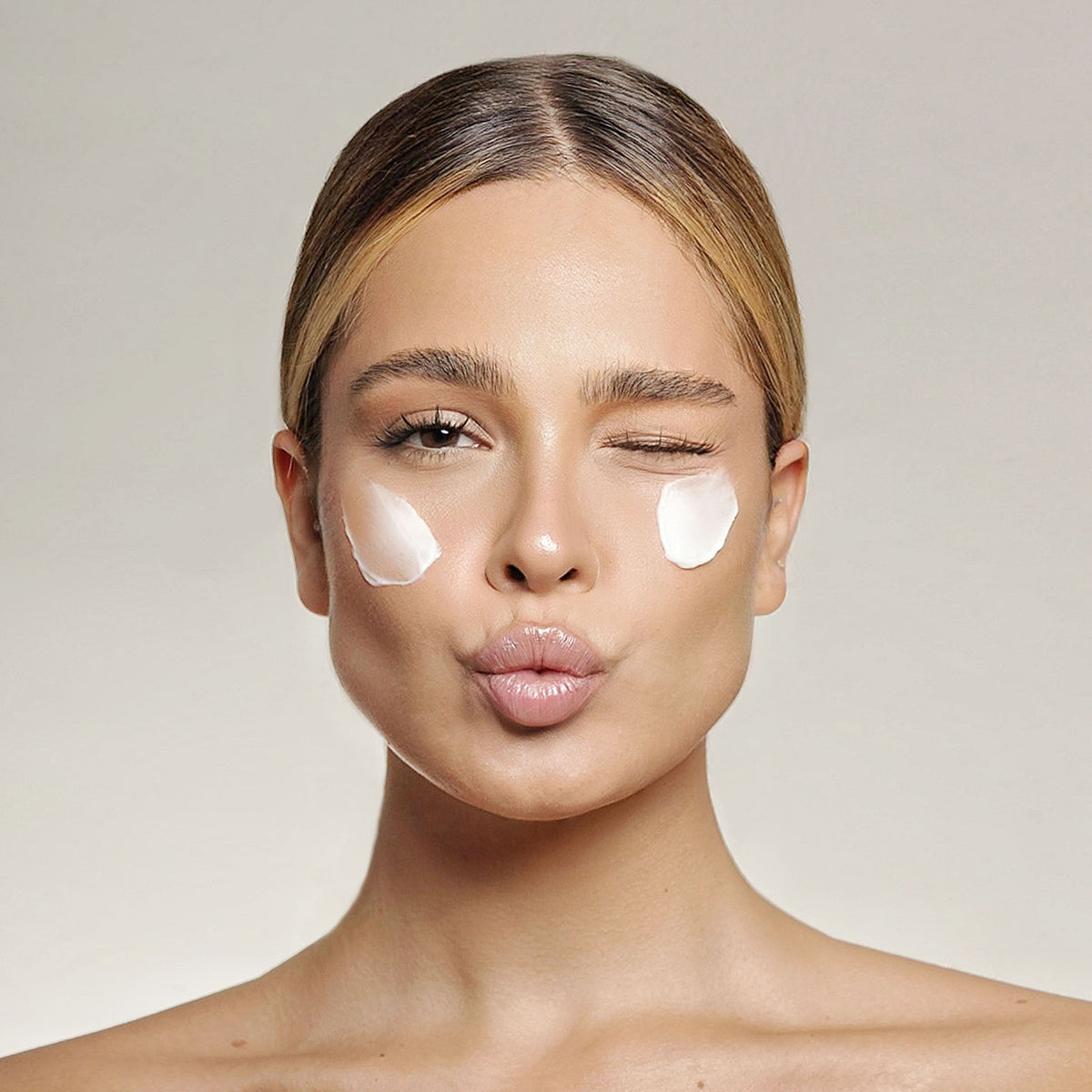 Cremă albă aplicată în puncte pe obraji, model care clipește, pentru Crema Antirid Natural Beauty by Laura Baldini.