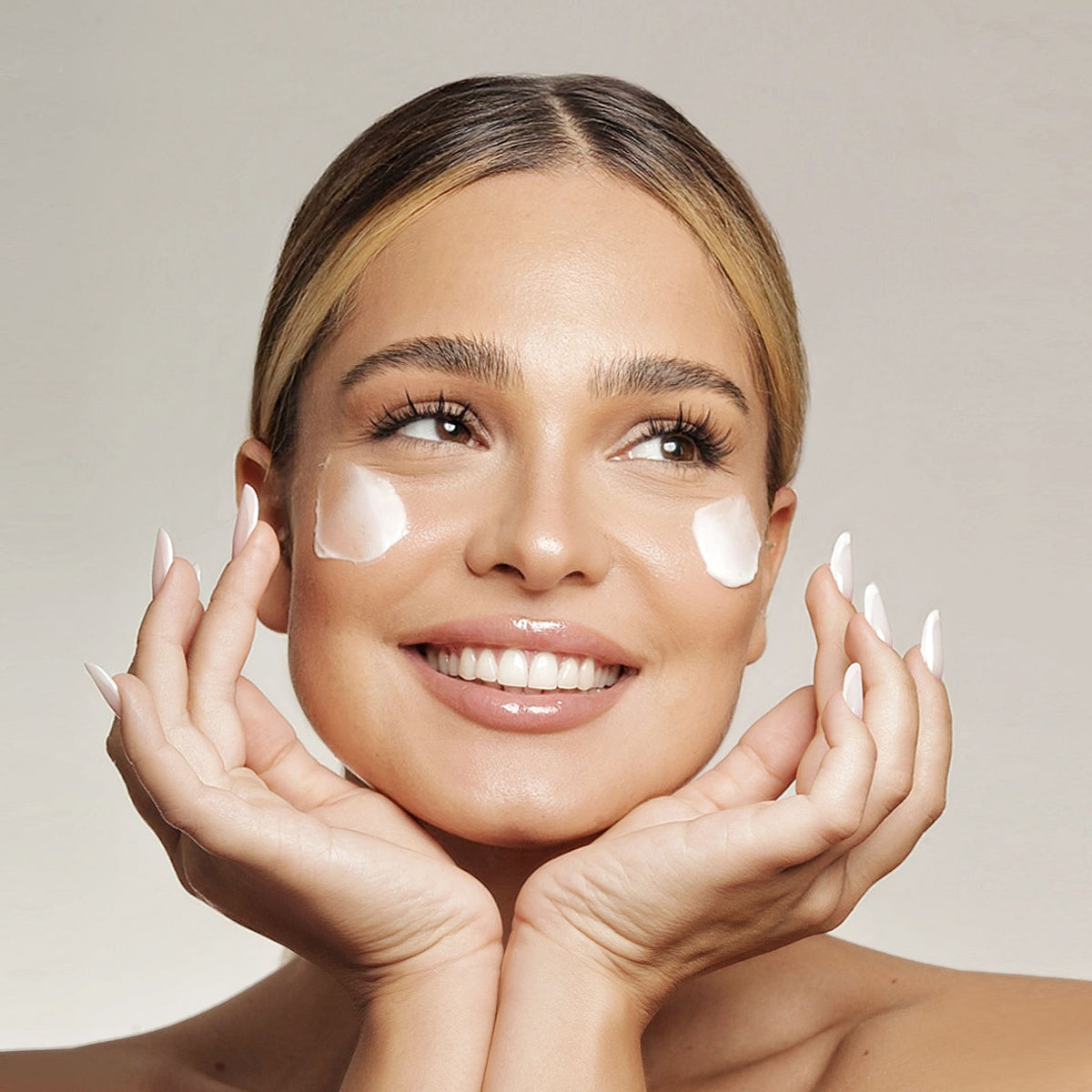 Model zâmbind, cu mâinile la față și cremă aplicată pe obraji, pentru Crema Antirid Natural Beauty by Laura Baldini.