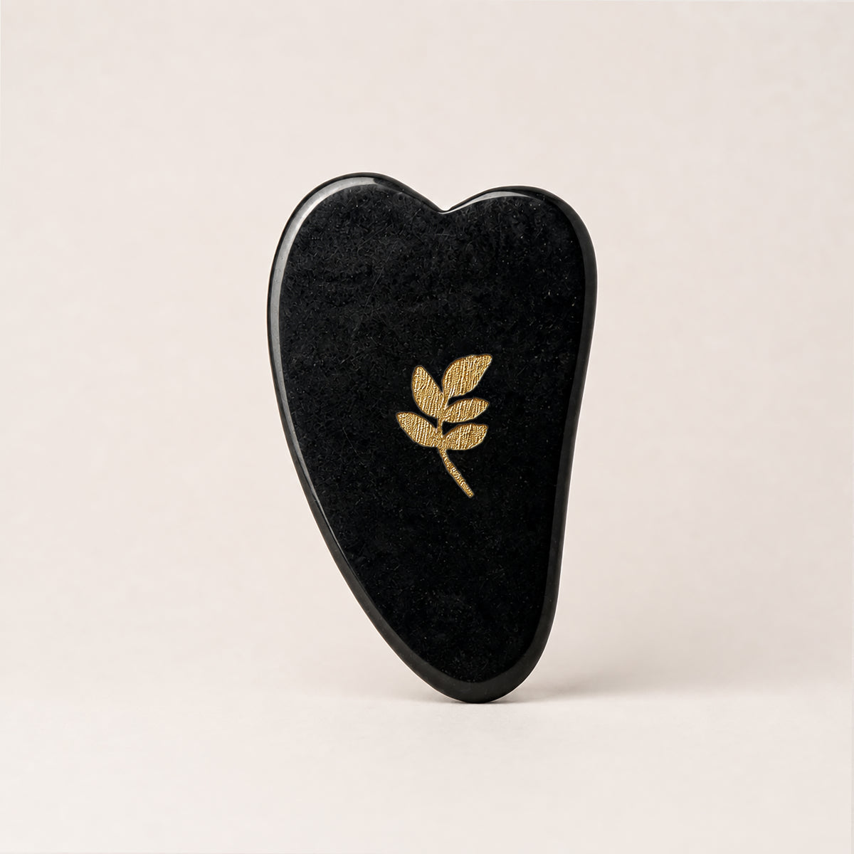 Gua Sha SCULPTIFY pentru masaj facial, din jad negru lustruit, în formă de inimă alungită, cu motiv auriu, așezat vertical