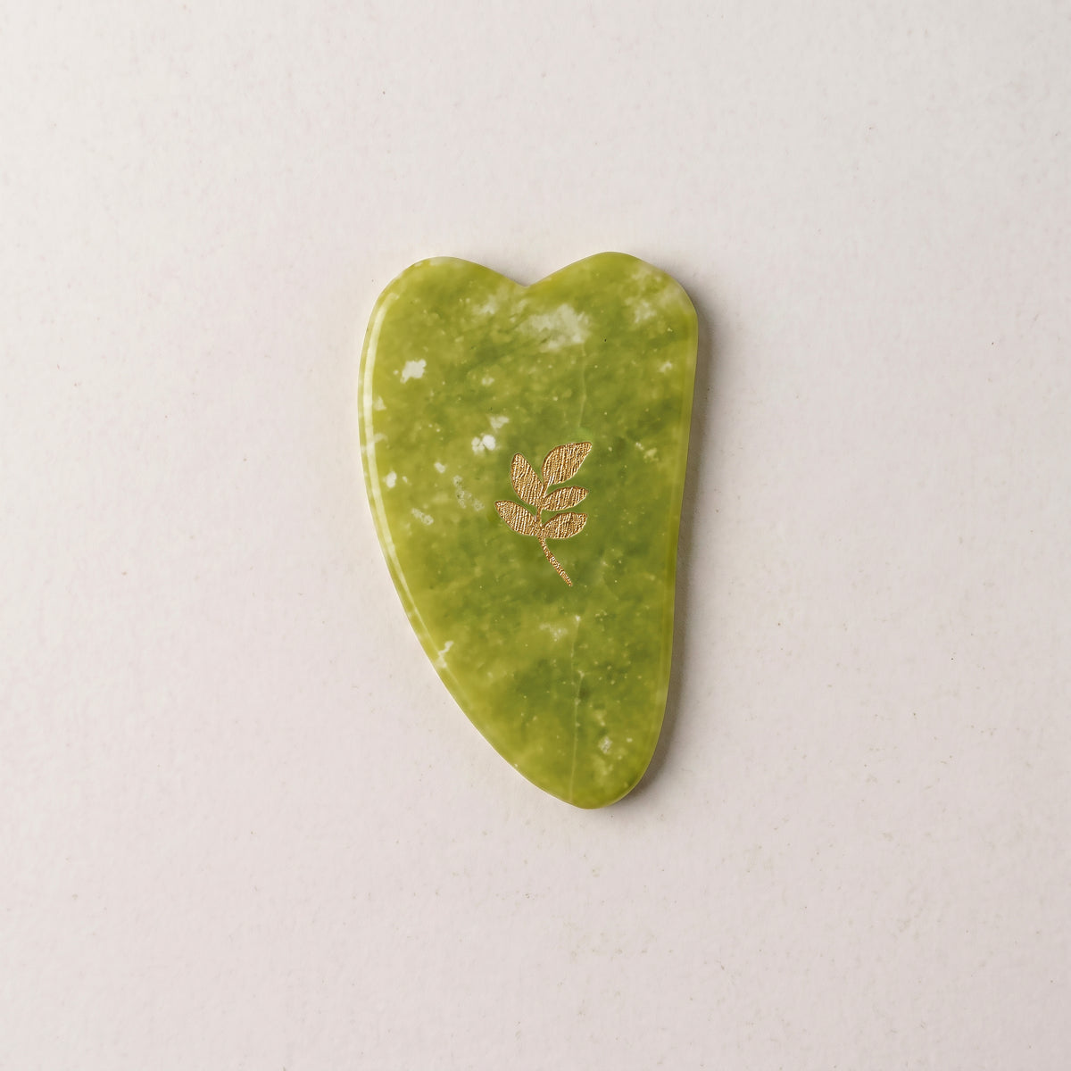 Gua Sha SCULPTIFY din jad verde cu pete albe naturale, în formă de inimă alungită, cu motiv auriu, așezat plat, văzut de sus